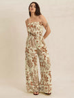Cream base jumpsuit with brown tropical print, wide legs, tie straps, smocked waist.