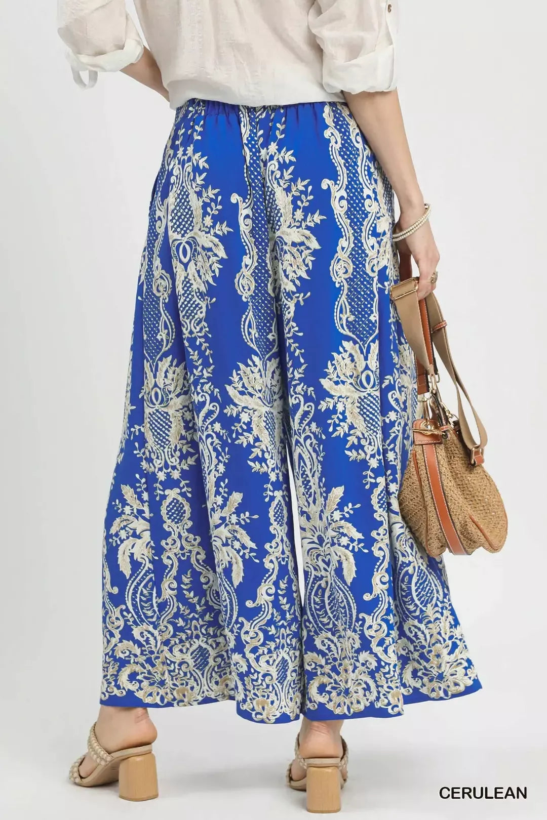 Flowy blue wide-leg pants with gold floral border print, high-waisted fit, paired with block-heel sandals