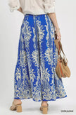 Flowy blue wide-leg pants with gold floral border print, high-waisted fit, paired with block-heel sandals