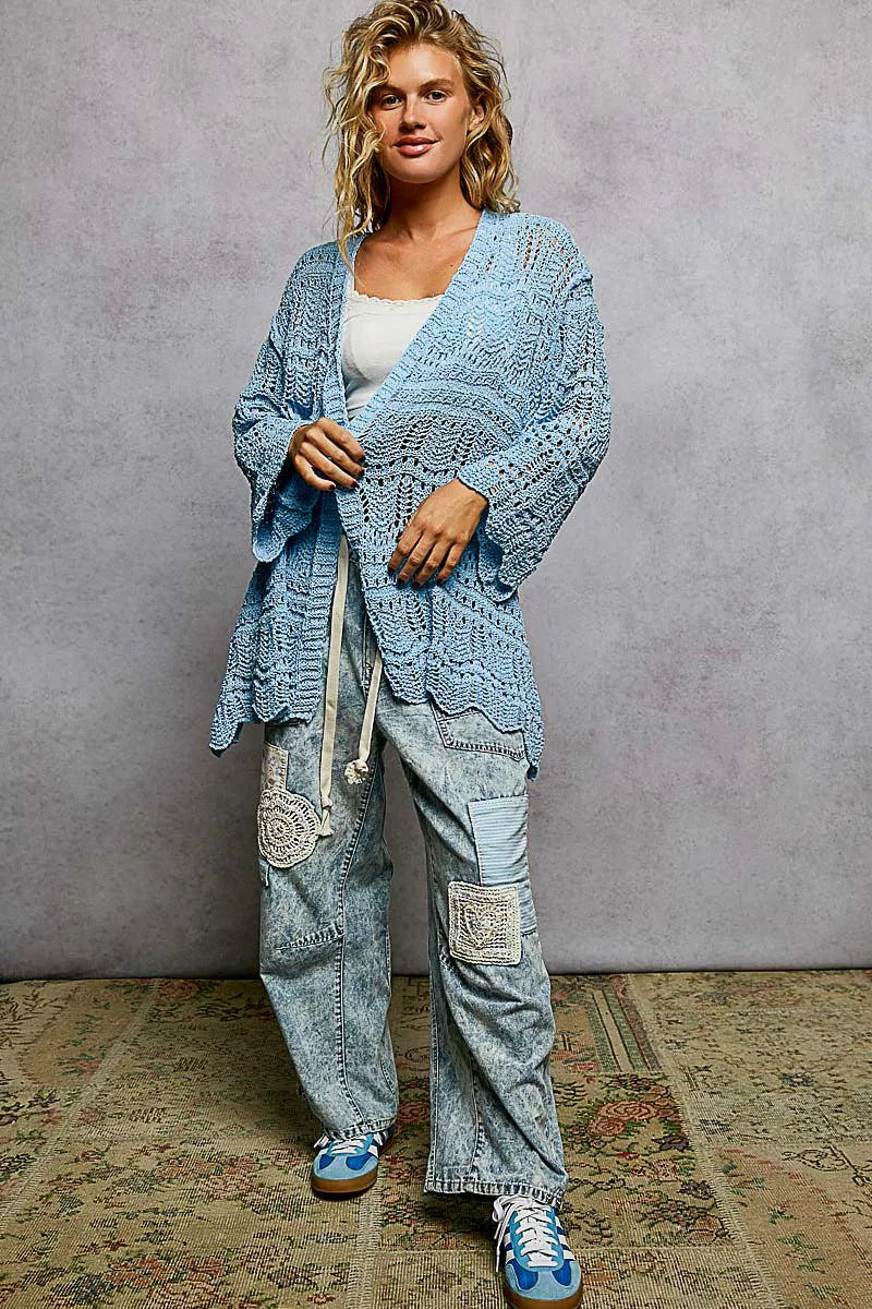 Light blue openwork cardigan with scalloped edge, loose fit, crochet texture, paired with distressed jeans.
