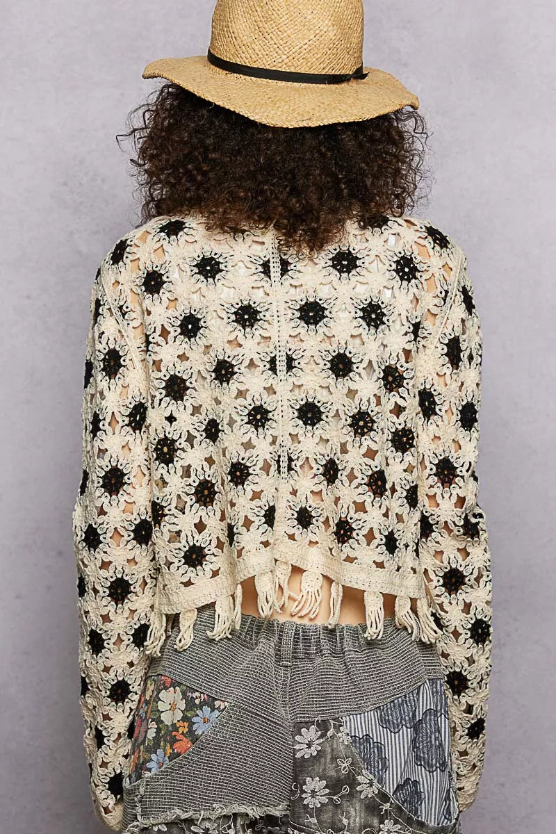 Cream and black openwork floral crochet cardigan with tassel hem, loose fit, textured fabric.