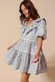 Light gray floral cotton dress with ruffled V-neck, puff sleeves, tiered skirt, and side tie waist.