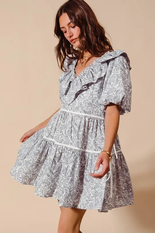 Light gray floral cotton dress with ruffled V-neck, puff sleeves, tiered skirt, and side tie waist.