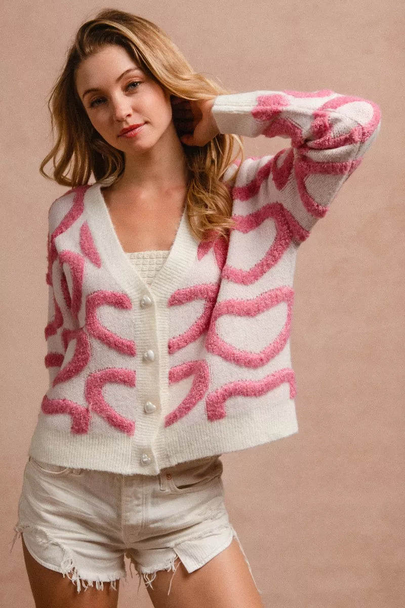 Pink and white textured heart pattern buttoned V neck cardigan with frayed denim shorts.
