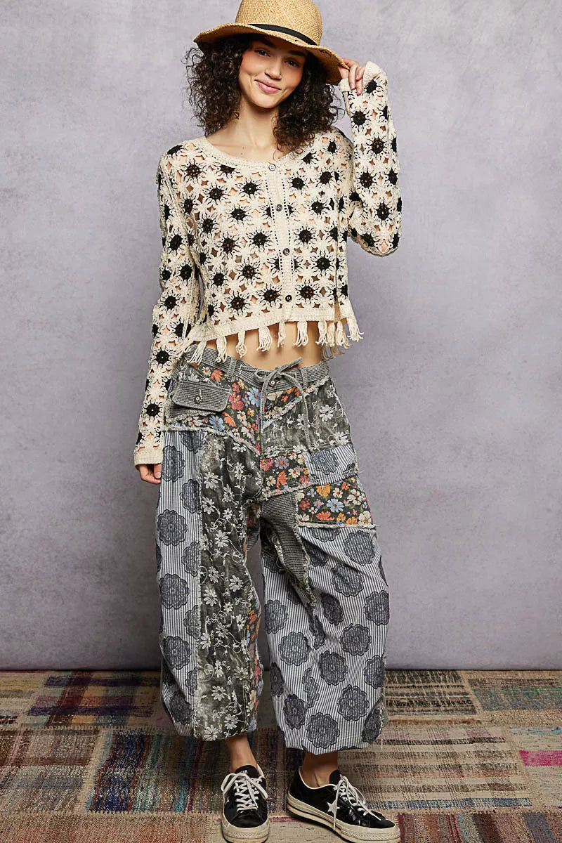 Cream crochet cardigan with black floral pattern, tassel hem, cropped fit, straw hat.