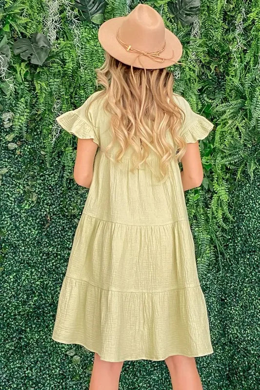 Pale yellow cotton gauze babydoll dress with ruffled tiered skirt and short sleeves worn with a wide-brim hat