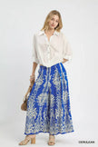 Flowy wide-leg blue pants with metallic damask print, paired with a crisp white button-up shirt.