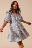 Woman wearing a white and gray cotton dress with ruffled V-neck and tiered skirt