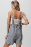 Light-wash denim shortall with ribbed top, open back, and patch detail.